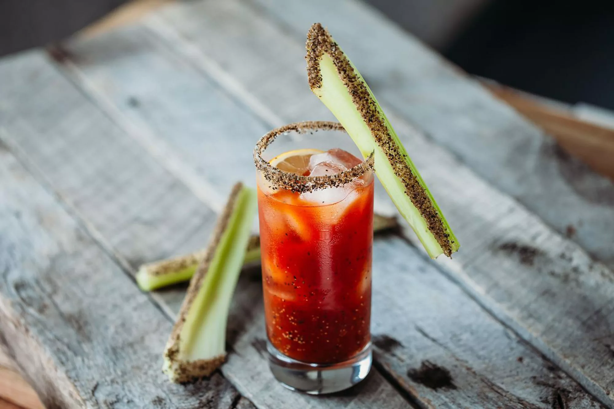 A bloody mary with celery sticks on a wooden table.